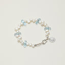 A close-up of the Azure Horizon bracelet featuring 3D teardrop Blue Topaz, luminous Baroque pearls, and an engravable sterling silver charm for personalized intentions.
