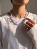 Model wearing the clear quartz and amethyst necklace with a white long-sleeve top.