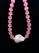 Close-up of pink cat’s eye beads and the baroque pearl centrepiece against a black background.