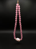 Full view of the pink cat’s eye and baroque pearl necklace hanging against a black background.