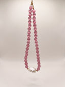 Pink cat’s eye and baroque pearl necklace hanging against a soft light background.