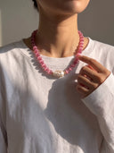Model wearing the pink cat’s eye and baroque pearl necklace with a white long-sleeve top.