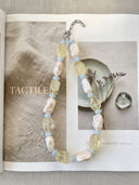Baroque pearl, citrine, and aquamarine necklace styled across an open editorial book.
