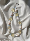 Citrine, aquamarine, and baroque pearl necklace displayed on white silk in natural sunlight.