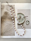 Trochus shell, red agate, and aquamarine necklace styled over an open editorial book.