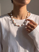 Model wearing the red agate, aquamarine, and trochus shell necklace with a white long-sleeve top.