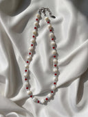 Trochus shell, red agate, and aquamarine necklace displayed on white silk in natural light.