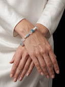 Elegant close-up of the Yuè TerraBrio Azure Resonance bracelet on a model's wrist against white silk, showcasing the luminous aurora pearls.