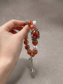 Hand holding the Yue TerraBrio Crimson Garden bracelet with red hematoid quartz beads, shell pearl, aged titanium steel floral details, and dangling charms.
