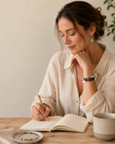A woman wearing meaningful gemstone jewelry while journaling in a calm modern daily ritual setting for Yue TerraBrio.