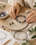 Close-up of hands arranging gemstone bracelet, pearl earrings, beads, linen, and jewelry sketch for a modern mindful jewelry ritual.